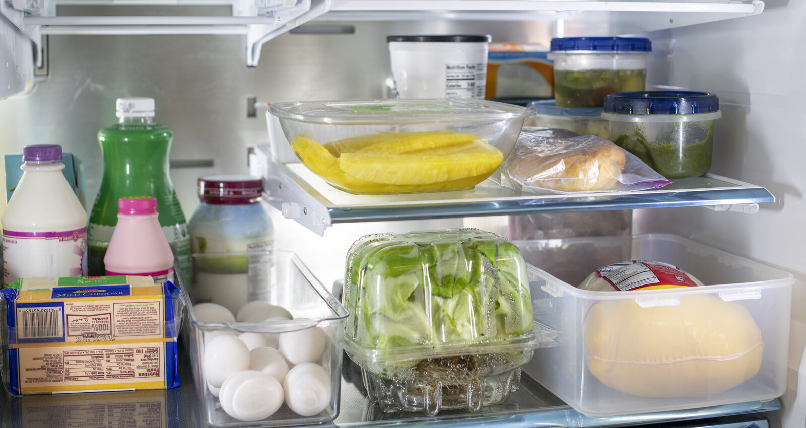 A real refrigerator containing sealed leftovers, dairy, eggs, produce, bread, and cheese